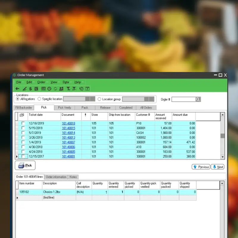 A computer screen displays an order management software window with a list of orders, item numbers, and quantities, supporting efficient grocery accounting. In the blurred background, colorful fruits and vegetables are on display.